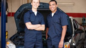 Two mechanics from The Bridge Auto standing in front of a car, smiling.